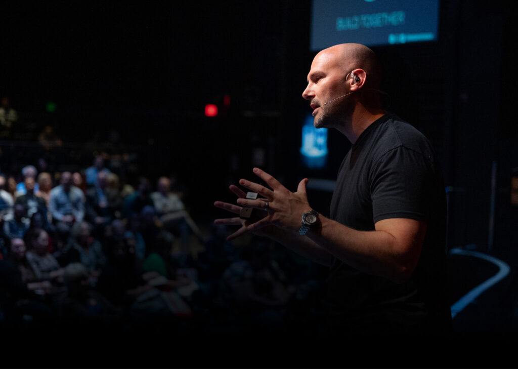 Employee Engagement Speaker Greg Offner standing in front of an audience with his hands outstretched as he talks